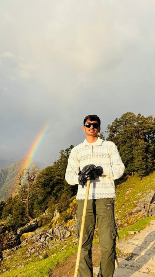 Parth on a stone mountain path in Uttarakhand with a rainbow over the valley